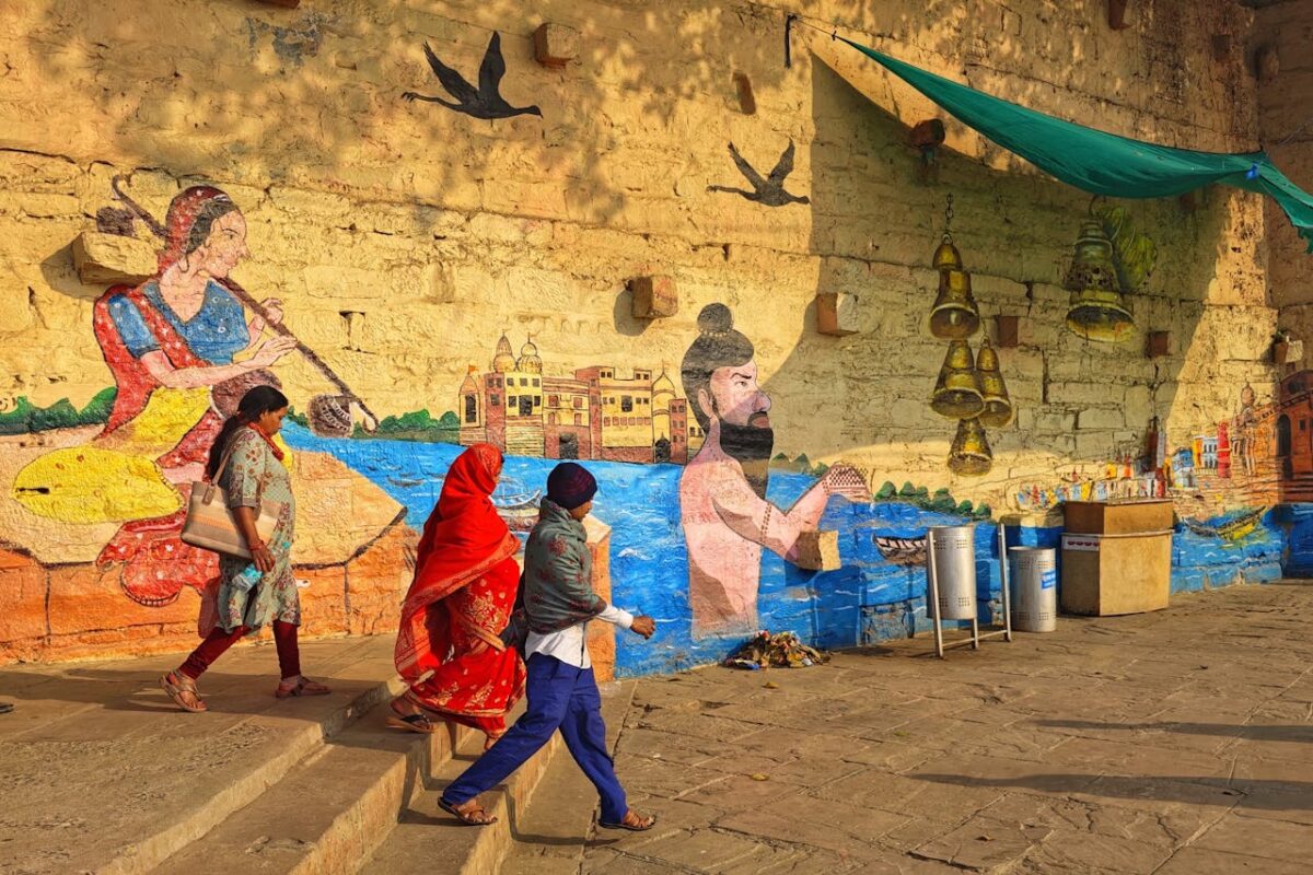 Colorful street art on a Varanasi wall with people passing by in traditional attire.