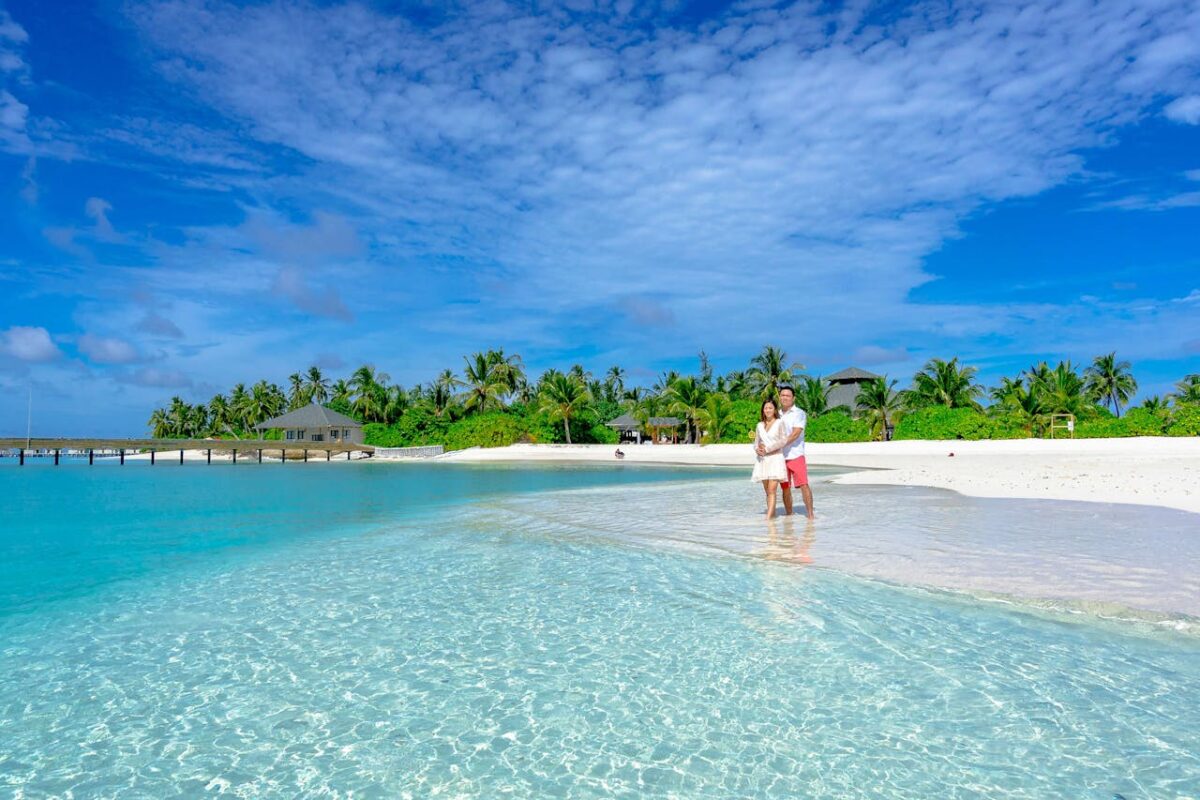 Couple embracing on a pristine Maldivian beach with clear waters and palm trees.